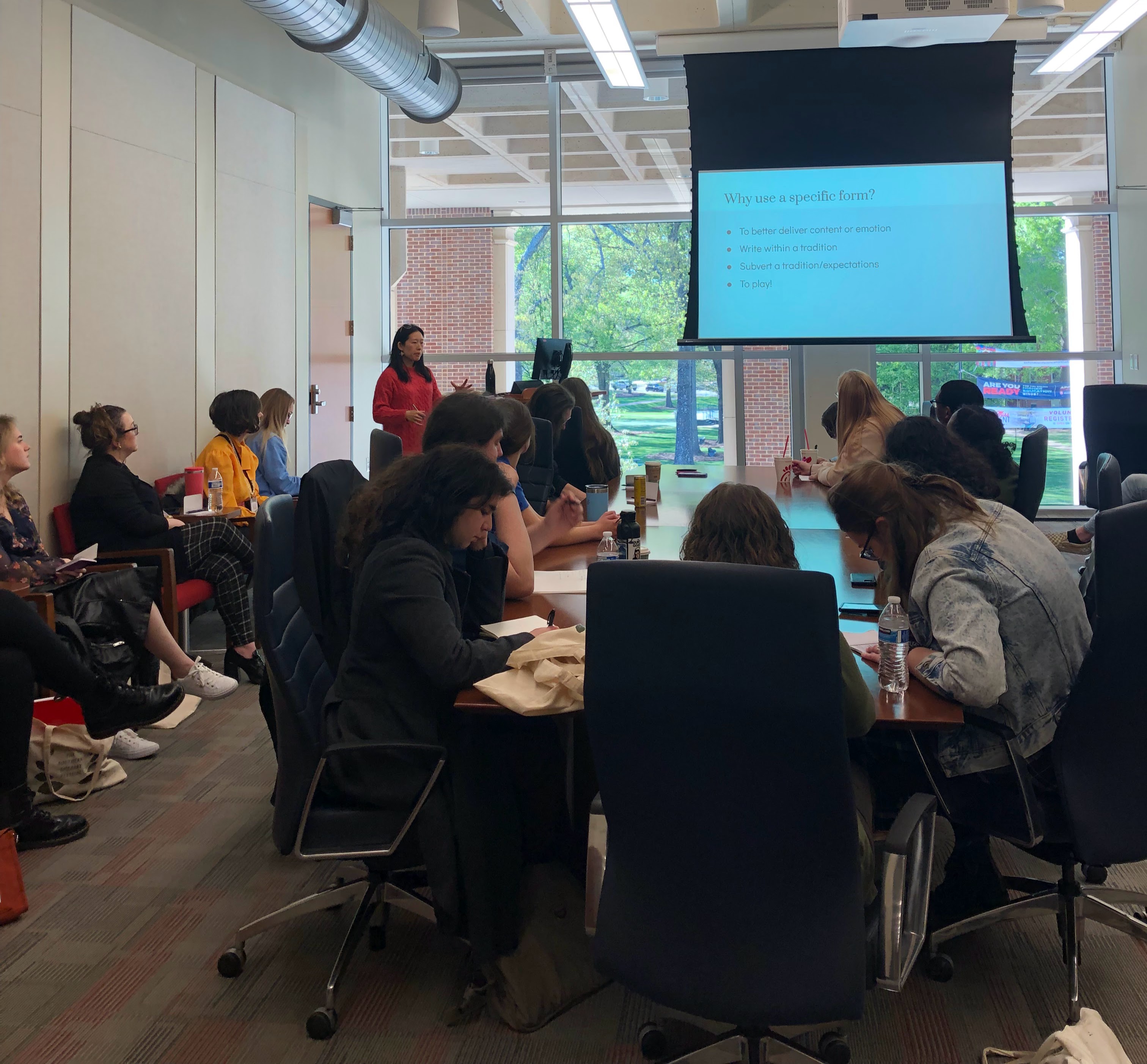 A classroom filled with students, some of whom have their heads down over the table as they take notes while others look up at a slide entitled "Why use form?"